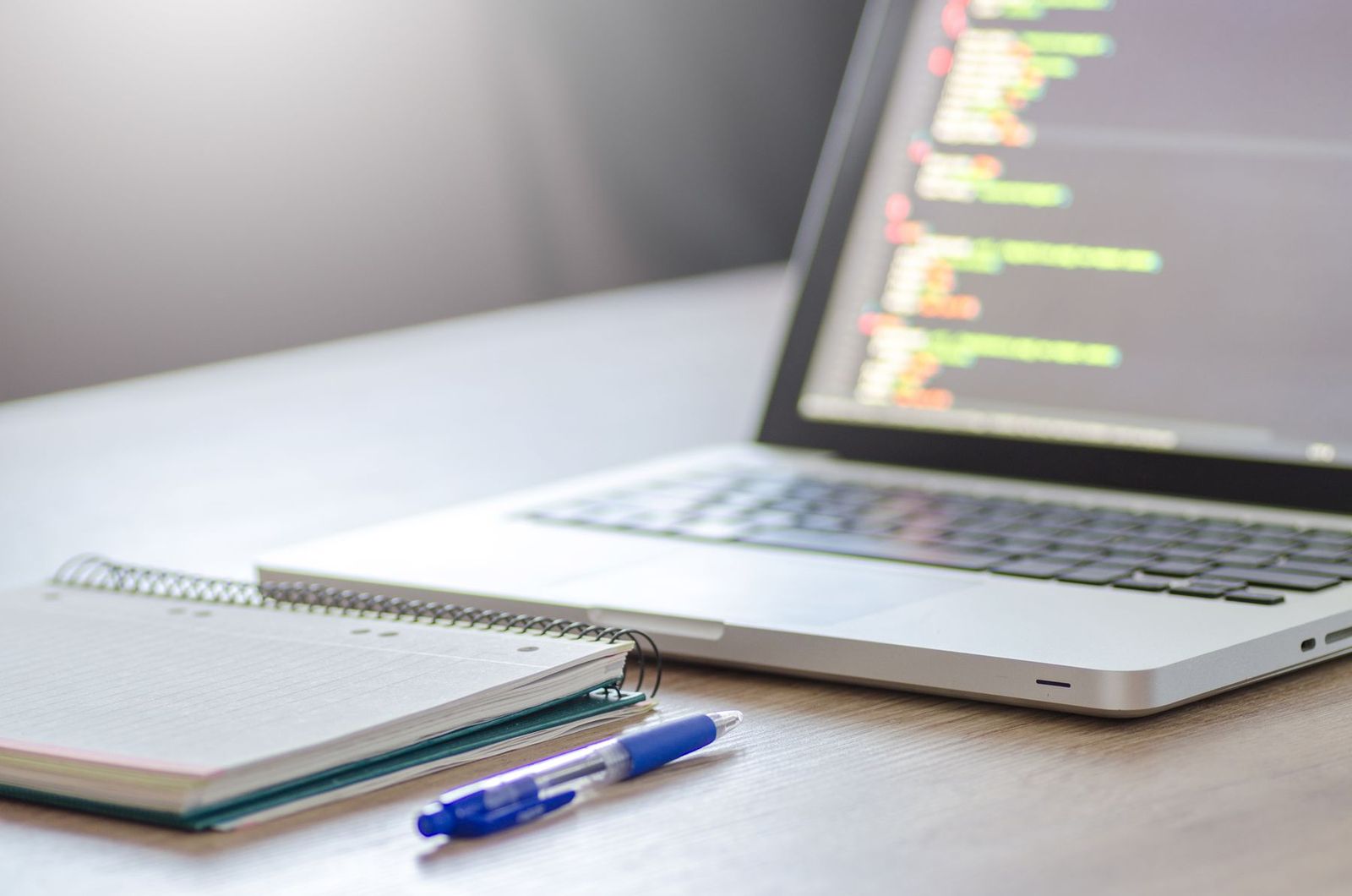Notebook aberto com código ao lado de caderno e caneta