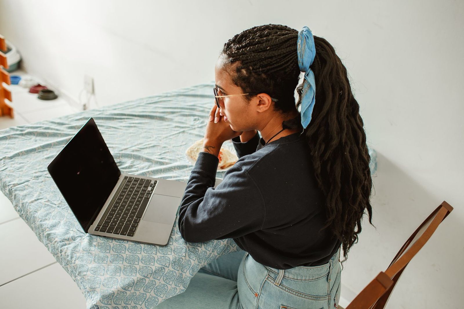Jovem de tranças e óculos estudando no notebook em casa